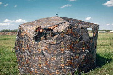 Good shot standing in ambush in the khaki tent, aiming to the sky; huntsman concept.