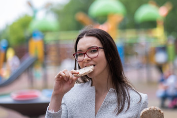 Young woman in glasses and a gray business suit is having a snack on the street. The girl adheres to proper nutrition and eats on a schedule. Diet crackers.