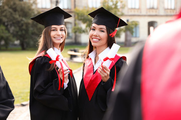 Happy students with diplomas outdoors. Graduation ceremony