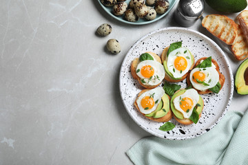 Flat lay composition of tasty bruschettas with quail eggs and avocado on light grey marble table, space for text