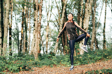 Morning exercise in the forest. Young woman stretches muscles after training. Portrait of a positive happy caucasian sportswoman.