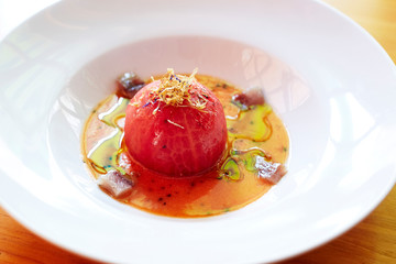 Peeled tomato with fish broth and fish on a white plate on a wood