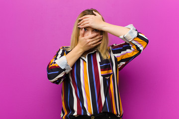 young blonde woman covering face with both hands saying no to the camera! refusing pictures or...