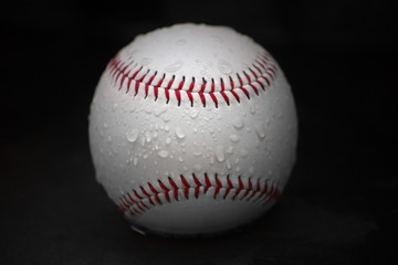 Baseball Ball with Red Seams and Water Droplets on Black Background. Closeup.