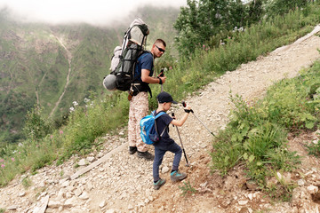 Obraz premium Father helps little son to go on his first mountain trip. Climb the mountain trail.