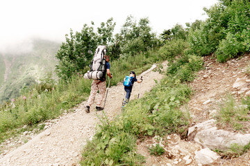 Obraz premium Dad and son hiking with heavy backpacks climb a mountain trail. Parenthood
