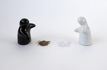 Ghost shaped salt and pepper shakers facing each other on poured out salt and pepper background,...