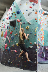 Young active woman with long hair grabbing by artificial rocks on climbing wall
