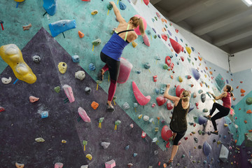 Obraz na płótnie Canvas Three young sporty women in activewear grabbing by rocks on climbing equipment