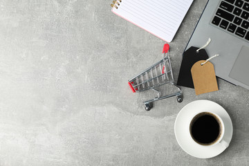 Composition with small shopping cart, laptop and cup of coffee on grey background, copy space