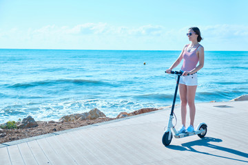 Young woman with electric scooter on a sea coast