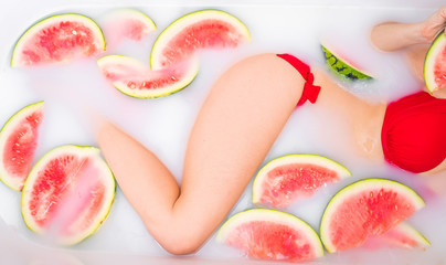 A woman takes a milk bath with slices of watermelons. SPA skin care treatments. Girl in a red...