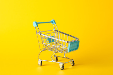 Small shopping cart on yellow background, space for text