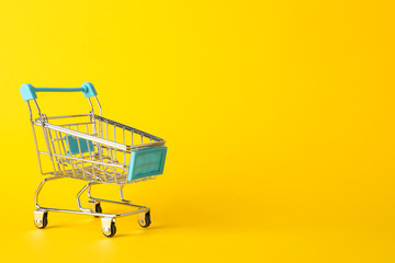 Small shopping cart on yellow background, space for text