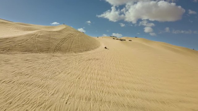 Aerial lateral of dune buggies driving on sand dunes in California