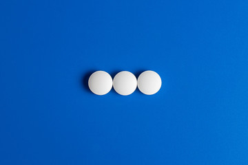 three white round pills on a blue background