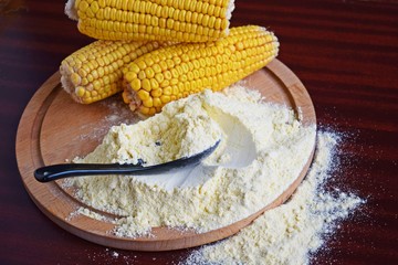 Corn flour and fresh cobs on a wooden background.