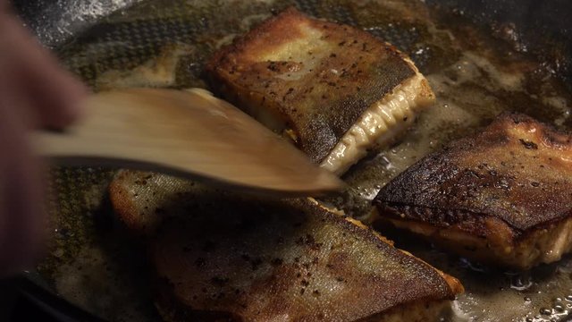 Roasting Arctic char fillet pieces in skillet. Butter and olive oil mix boiling in frying pan. Close up of cooking delicious meal from fish that taste is like something between trout and salmon.