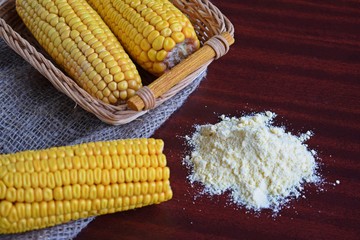 Corn flour and fresh cobs on a wooden background.
