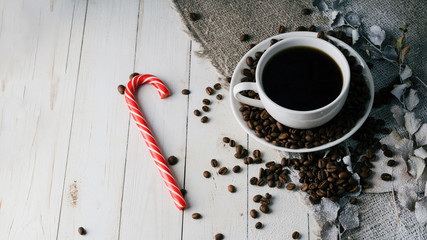 A hot cup of coffee with a candy and the coffee beans on the table in a cafe. Composition of a delicious coffee and sweet snack.