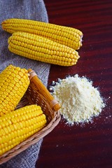 Corn flour and fresh cobs on a wooden background.