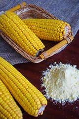 Corn flour and fresh cobs on a wooden background.