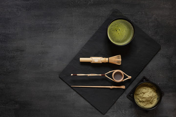 Matcha green tea ceremony kit - matcha powder, wooden spoon, strainer and whisk on a dark gray background