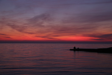 silhouette of a fisherman at sunset. Bright colors of the sunset. Red sunset.