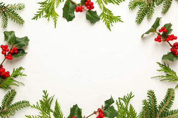 Christmas background with branches of fir tree, evergreens and holly with red berries on white. Winter nature concept. Flat lay, copy space.