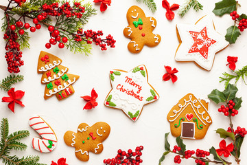Christmas background with gingerbread cookies and branches of holly with red berries on white. Winter festive nature concept. Flat lay, copy space.