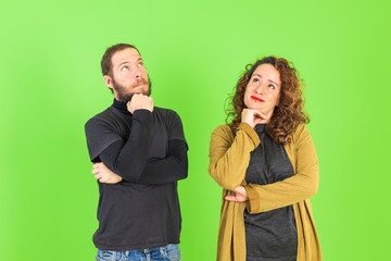 Young beautiful couple on isolated green background with hand on chin thinking about question, pensive expression. Smiling with thoughtful face. Doubt concept.