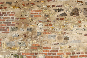 Old wall made of natural rocks and bricks partially coated with plaster
