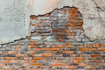 An old damaged brick wall partially covered with old cracked plasterwork