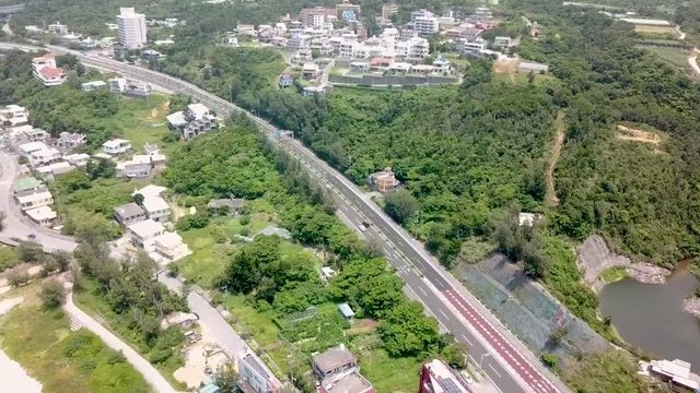 Flying forward above Onna, Okinawa, Japan. Drone footage over turquoise water. Flying over street and houses surrounded by the forest. White sand and blue water.