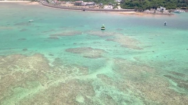 Flying forward above Onna, Okinawa, Japan. Drone footage over turquoise water. Flying over street and houses surrounded by the forest. White sand and blue water.