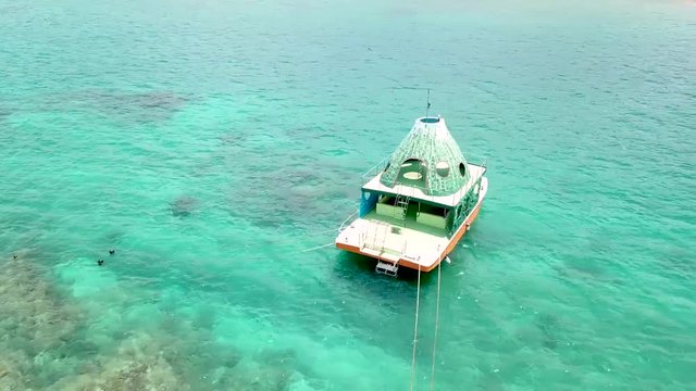 Flying forward above Onna, Okinawa, Japan. Drone footage over turquoise water. Flying backward over the ocean with a boat in the right. Rocks underwater.White sand and blue water.