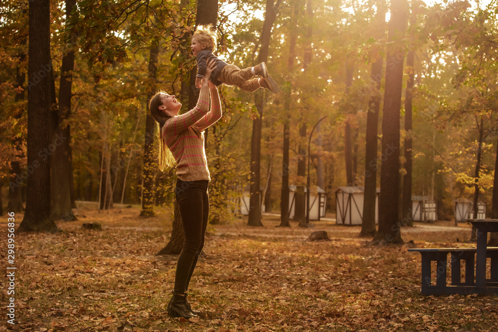 Wall mural Happy mom is circling with her beautiful baby in the autumn park. Lifestyle. Happy emotions. Play in the park.