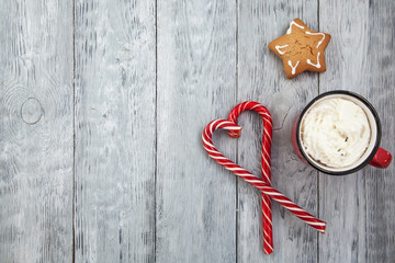 Red mag of drink with candy cane and Christmas gigerbread on wooden background. Copy space