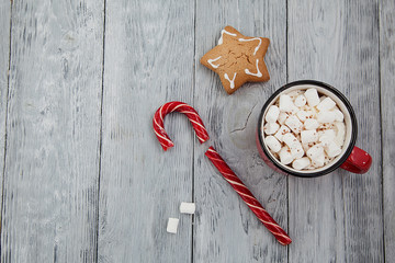 Red mag of drink with candy cane and Christmas gigerbread on wooden background. Top View.