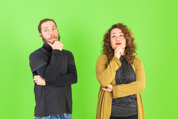 Young beautiful couple on isolated green background with hand on chin thinking about question, pensive expression. Smiling with thoughtful face. Doubt concept.