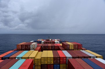 Container ship loaded with containers sailing through Pacific Ocean towards a stormy clouds. 