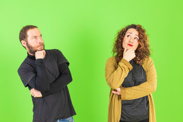 Young beautiful couple on isolated green background with hand on chin thinking about question, pensive expression. Smiling with thoughtful face. Doubt concept.