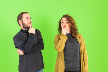 Young beautiful couple on isolated green background with hand on chin thinking about question, pensive expression. Smiling with thoughtful face. Doubt concept.