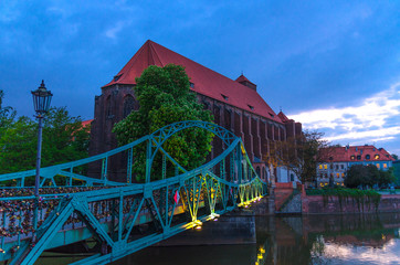 Roman Catholic parish Saint Mary church NMP on Sand island Wyspa Piasek, view through arch of Tumski bridge over Odra Oder river in old town historical city centre of Wroclaw, evening view, Poland