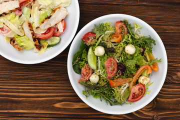 white deep plates with fresh salad ingredients mixed with sauce placed on a rustic background. A place for a menu, banner or advertisement