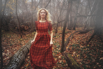 Young pretty woman in the red dress is walking in the foggy mystical forest