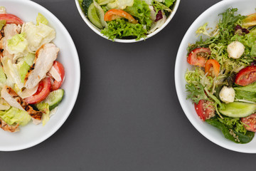 white deep plates with fresh salad ingredients mixed with sauce placed on an gray background. A place for a menu, banner or advertisement