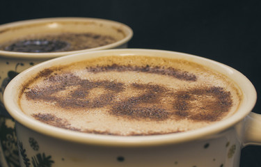 Mug of cappuccino with cinnamon for breakfast.Cinnamon powder is sprinkled with 2020 numbers on coffee foam. Cookie with a paw pattern floats in a cappuccino.Morning Cup of coffee with hot cappuccino.
