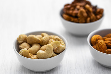 Cashews, almonds and walnuts in white bowls on a white wooden background, top view from the side
