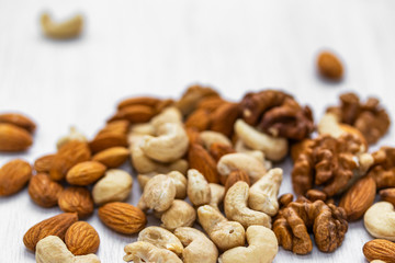 Almonds, cashews and walnuts scattered on a white wooden background, side view from above